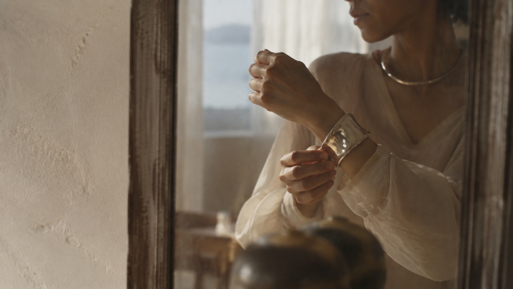 A person adjusting a silver cuff before a mirror